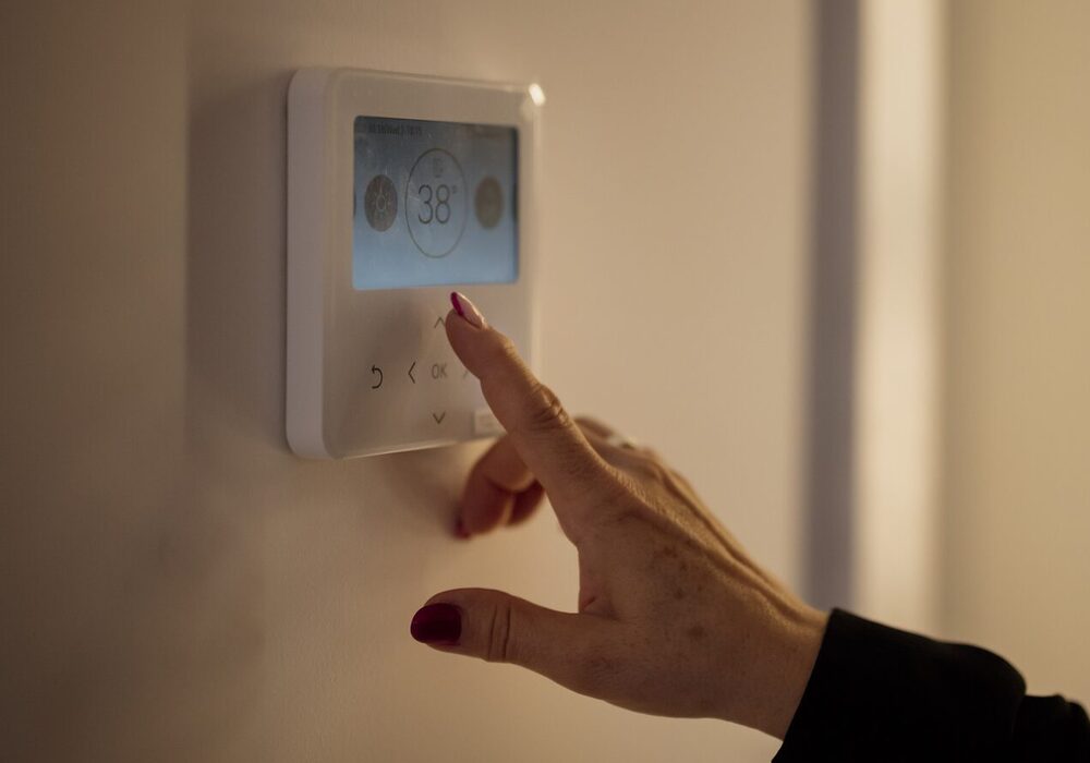A hand setting the temperature on a wall-mounted digital thermostat inside a home